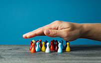 A hand hovering over a group of wooden people figurines.